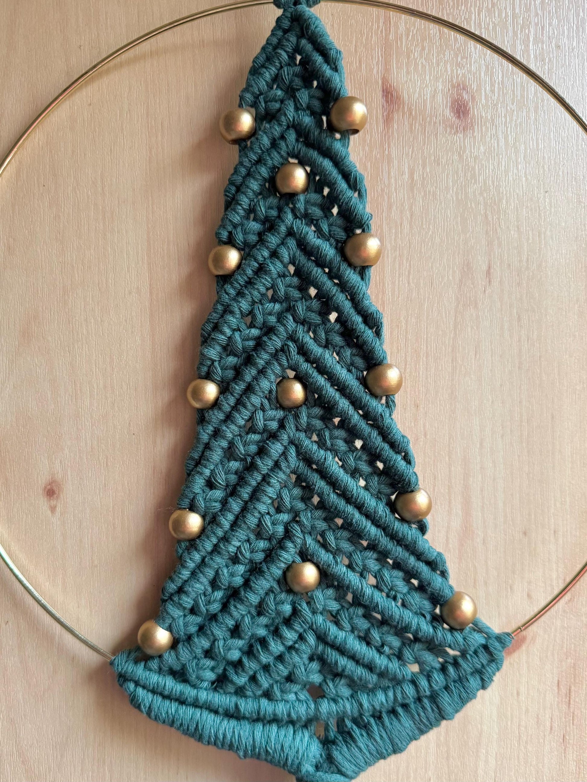 Dark green macrame christmas tree wall hanging with gold beads on a wooden surface
