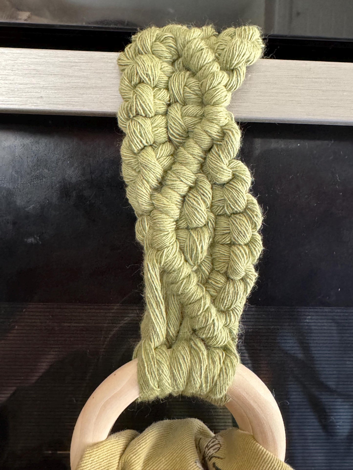 Green braided yarn on a wooden holder against a dark background