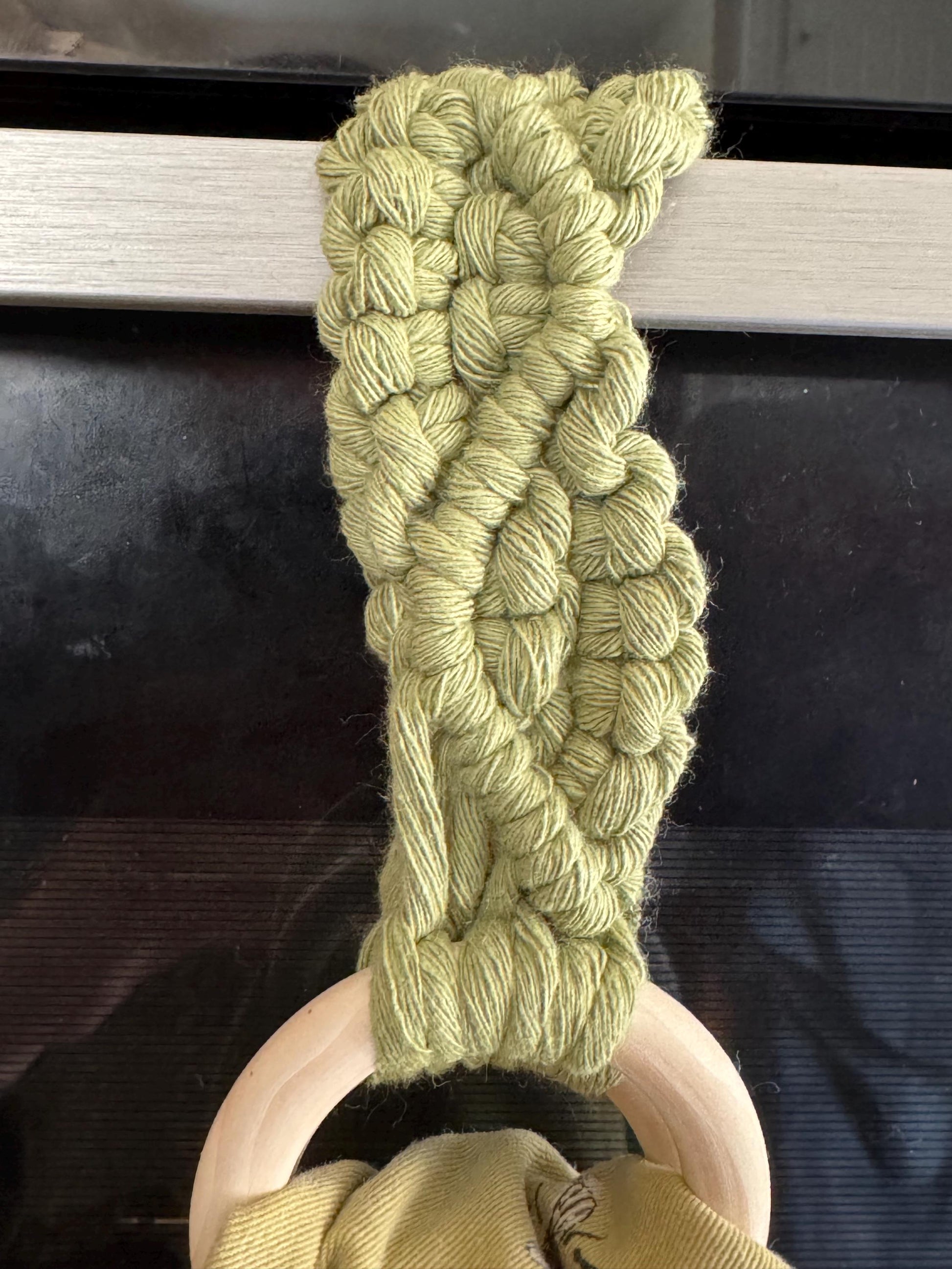Green braided yarn on a wooden holder against a dark background