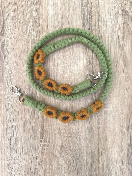 Green macrame strap with sunflower designs on a wooden surface