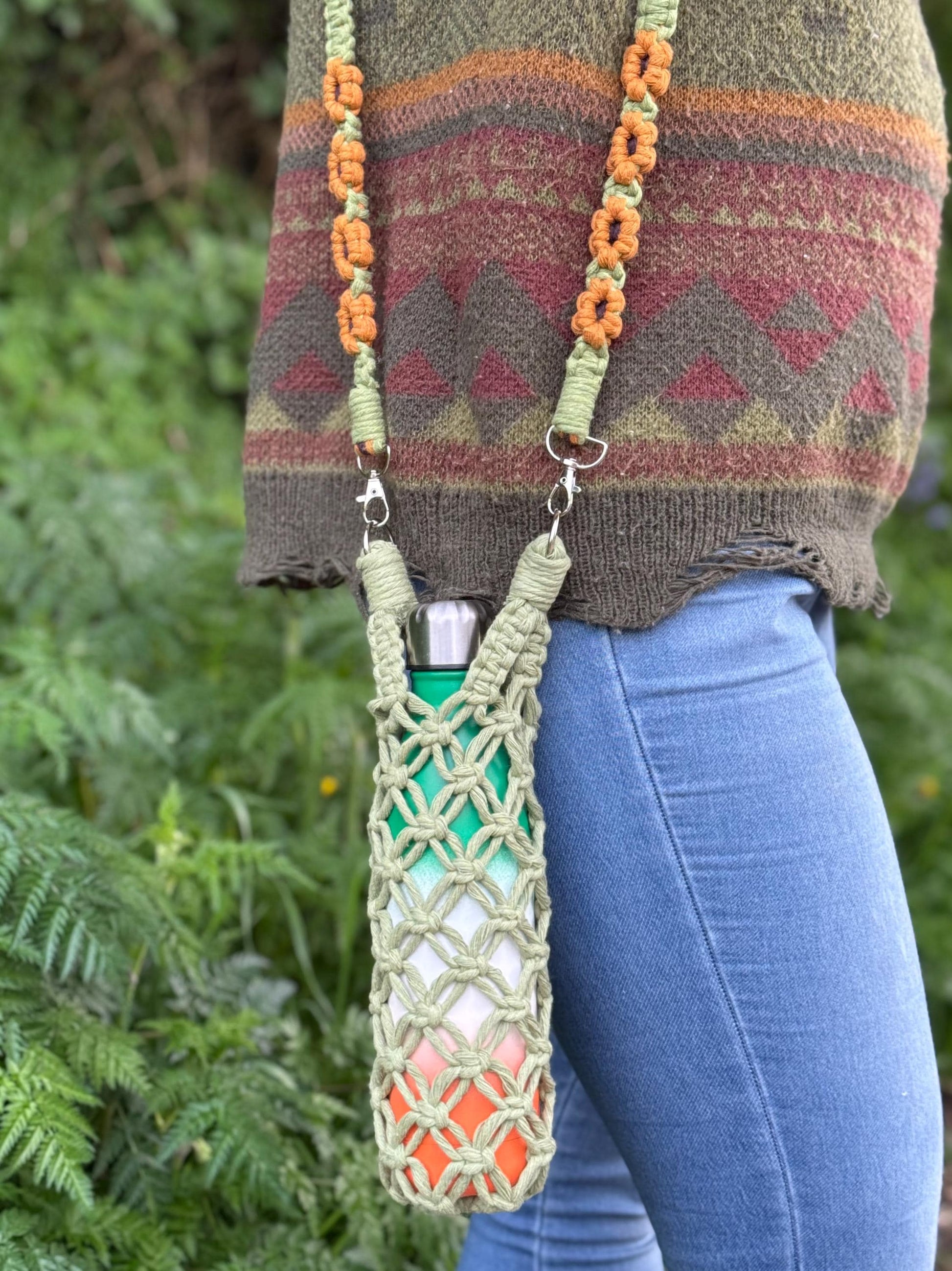 Person wearing a patterned sweater with a green macrame water bottle holder featuring a colorful sunflower strap.