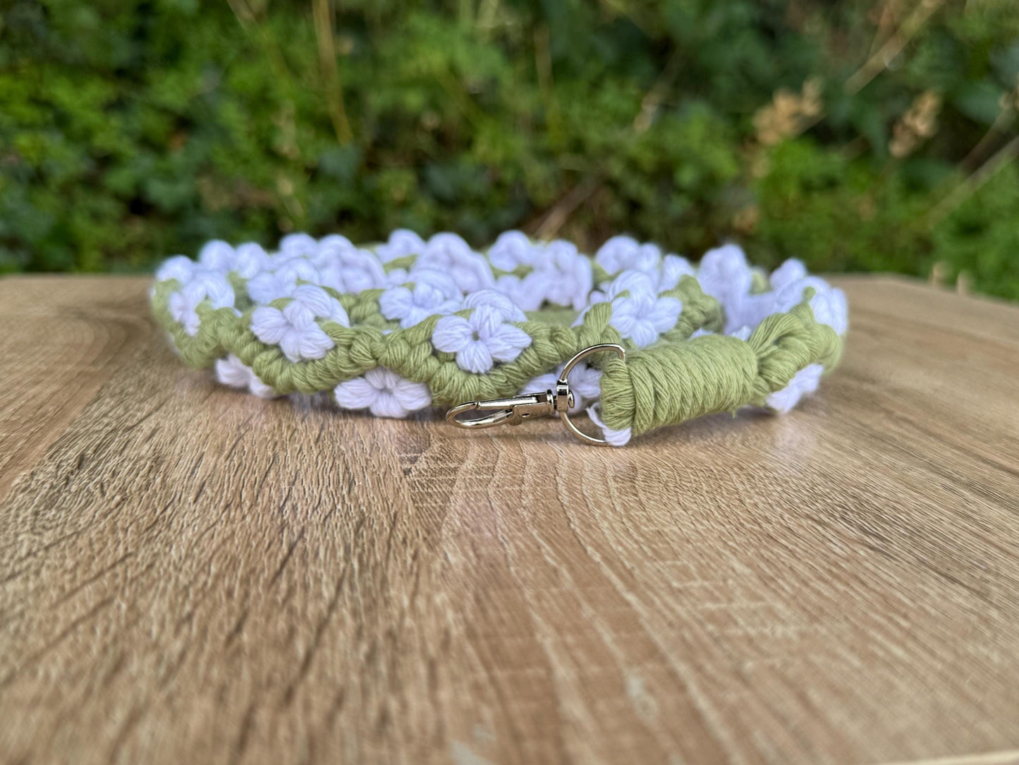 Green and white floral-patterned strap on a wooden surface with a blurred green background