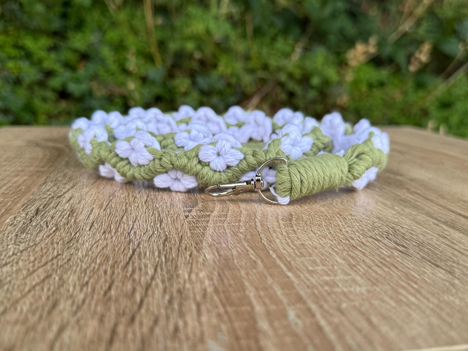 Green and white floral-patterned strap on a wooden surface with a blurred green background