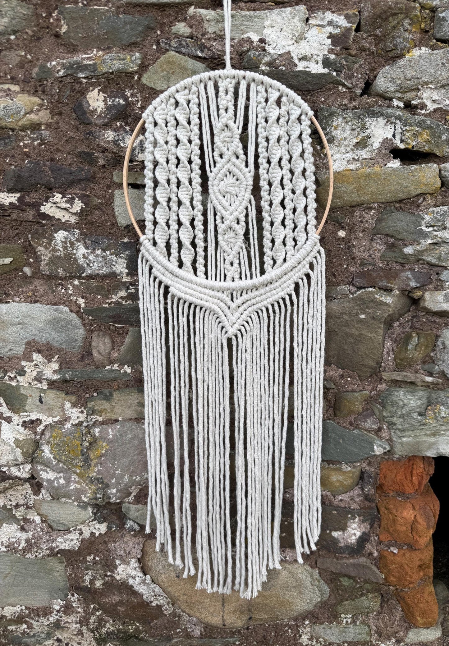 Macrame wall hanging with fringes against a stone wall background