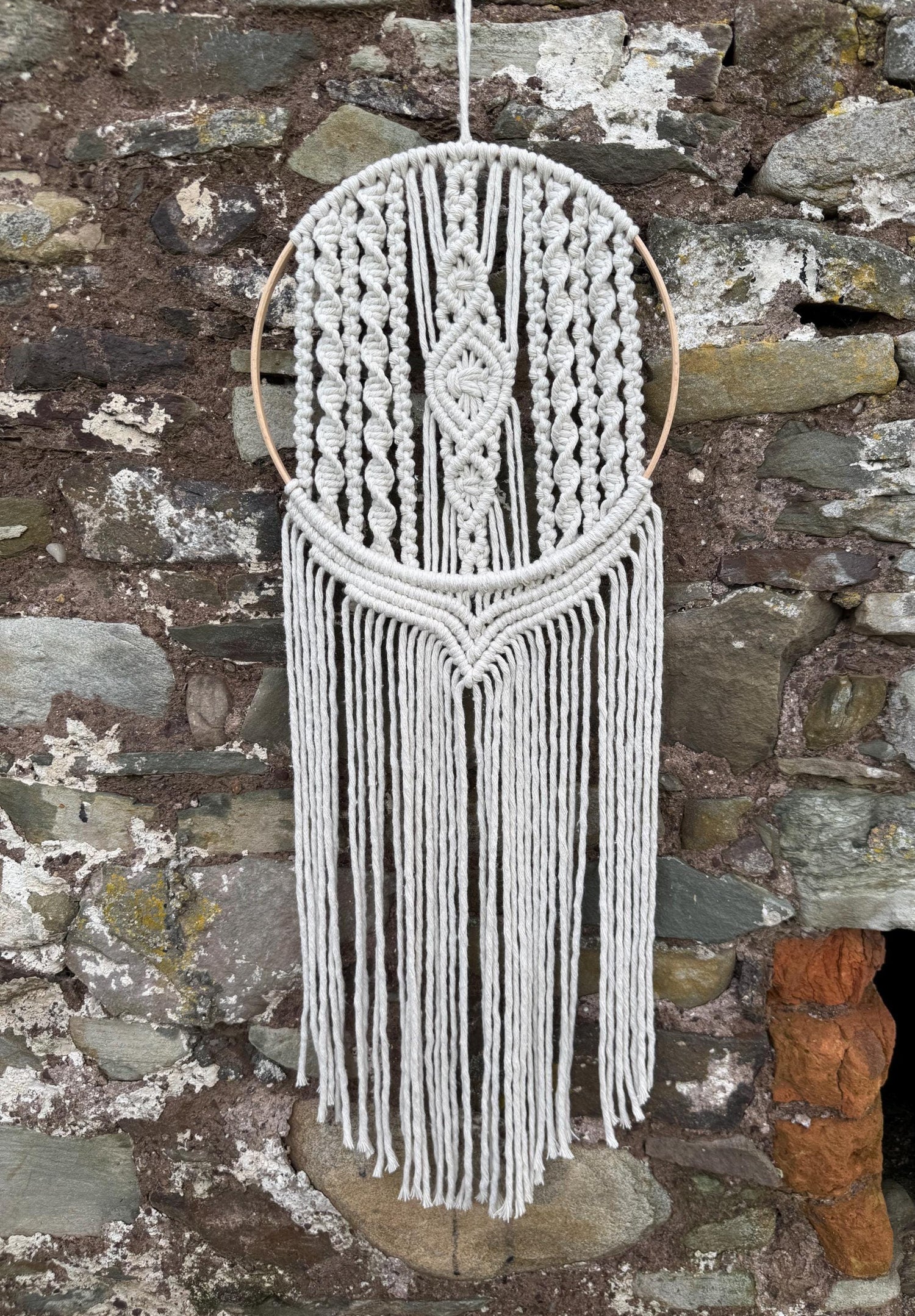 Macrame wall hanging with fringes against a stone wall background