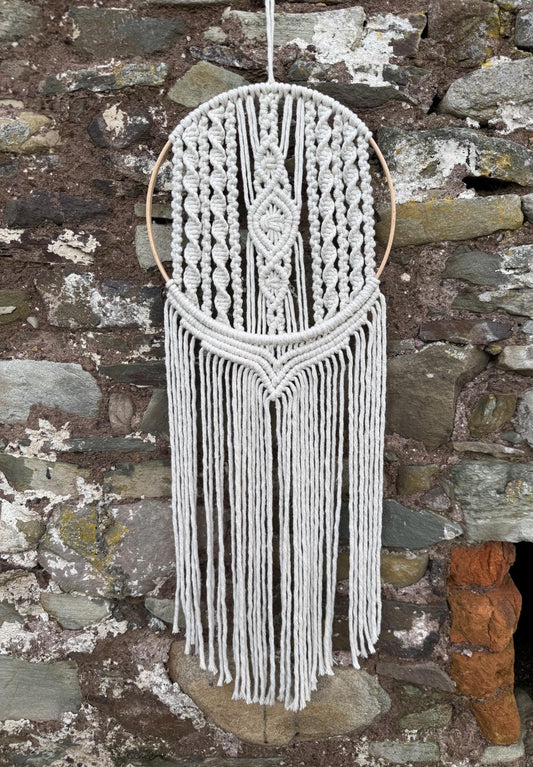 Macrame wall hanging with fringes against a stone wall background