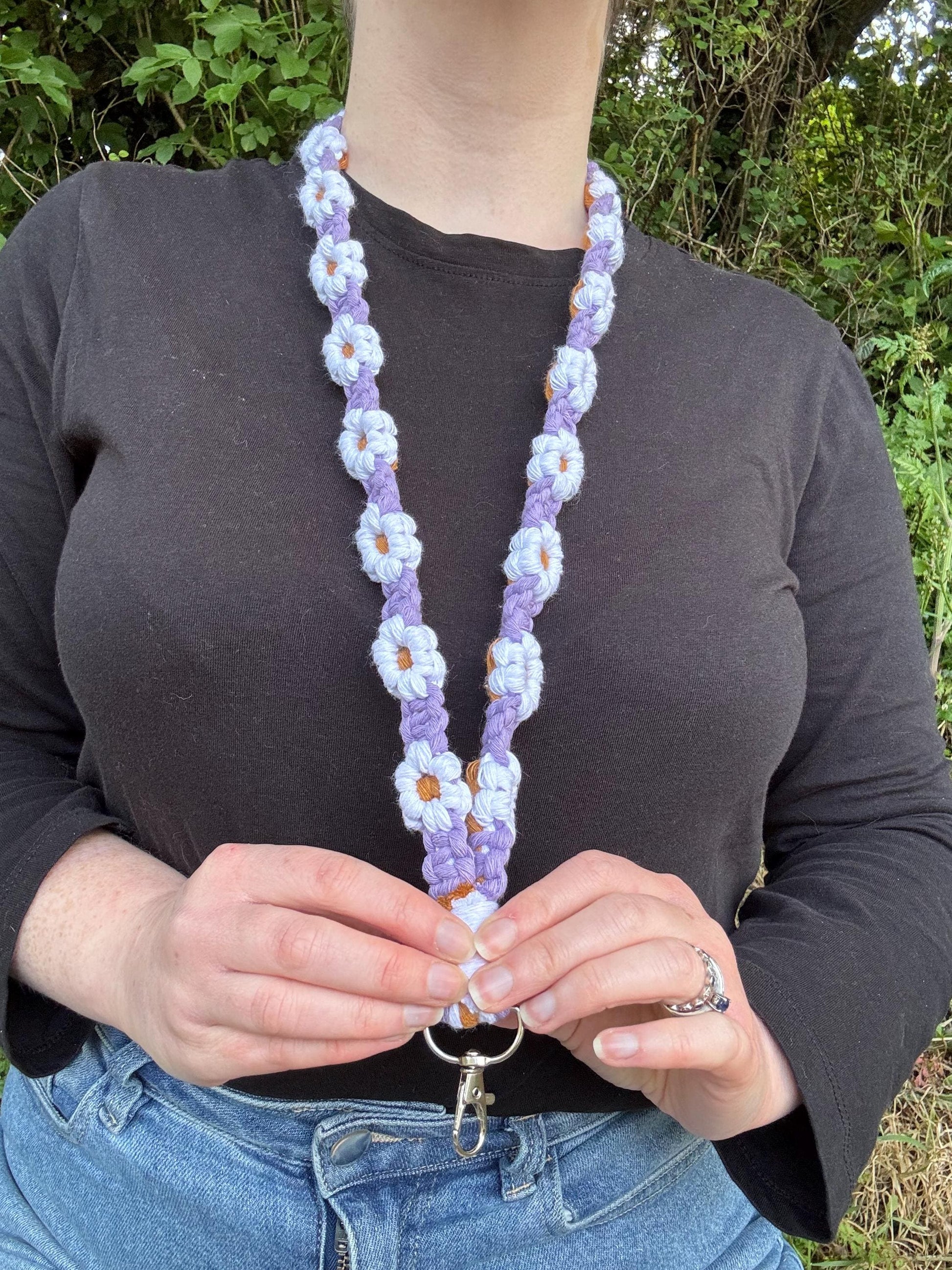 Person wearing a lilac macrame lanyard with daisy designs against a natural background