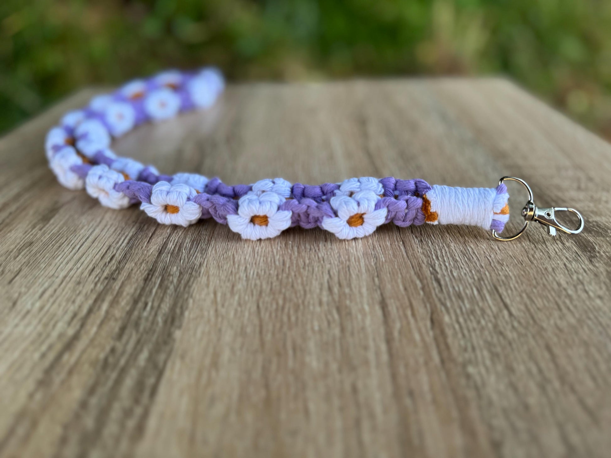 Handmade macrame lanyard with purple and white floral pattern on a wooden surface