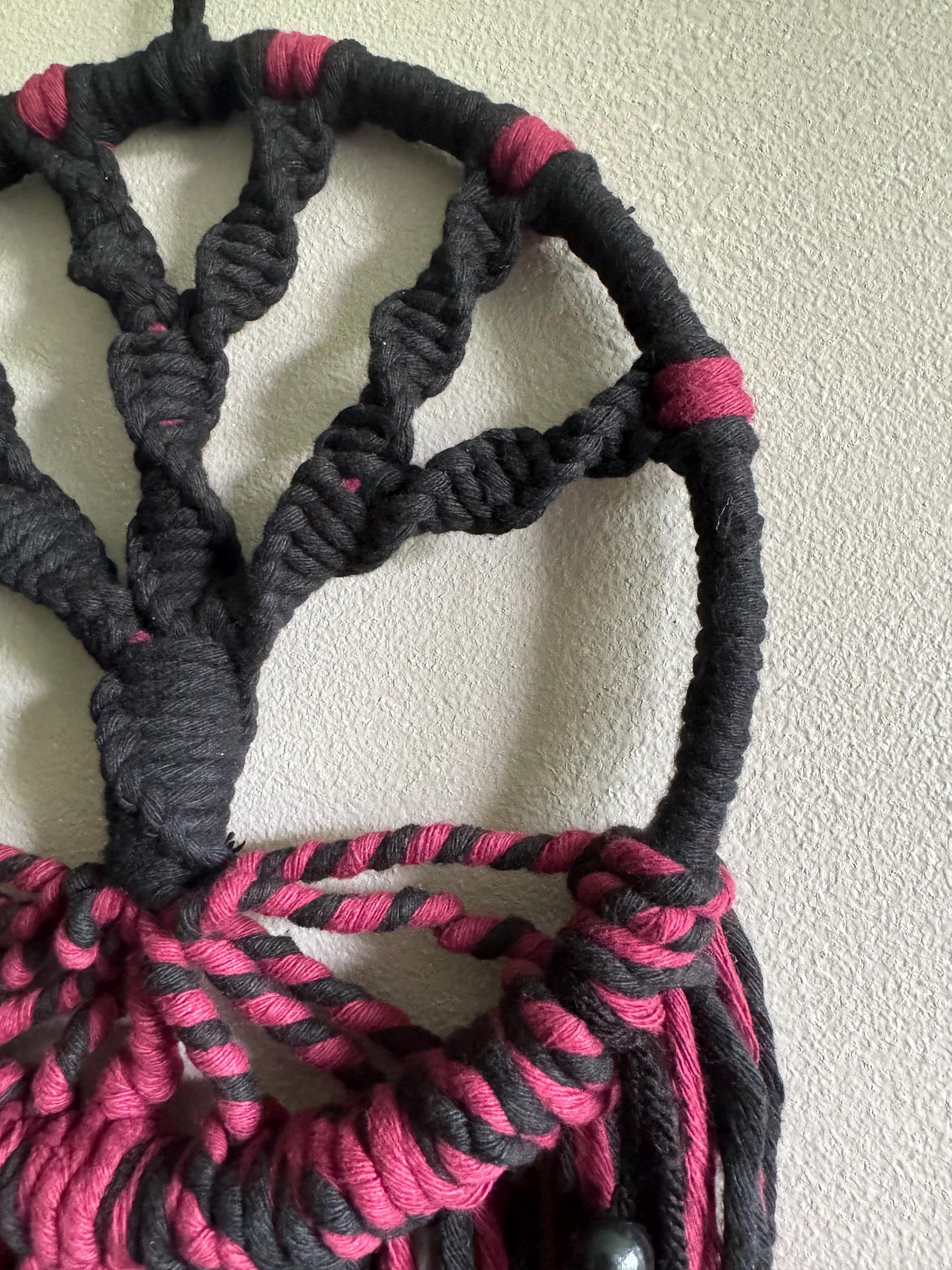Close-up of a black and burgundy macrame tree of ilfe wall hanging against a white wall.