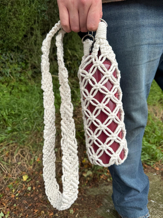 Person holding a macrame net bag with a bottle inside against a natural background