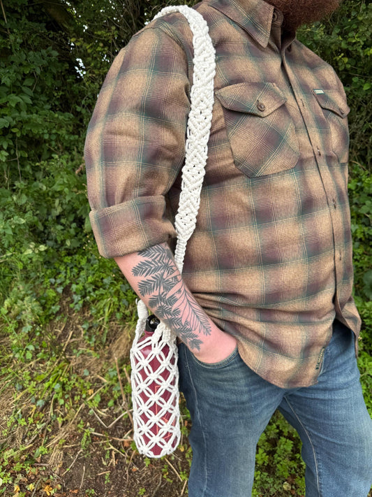 Person wearing a brown flannel shirt holding a white macrame water bottle holder with a detailed strap.