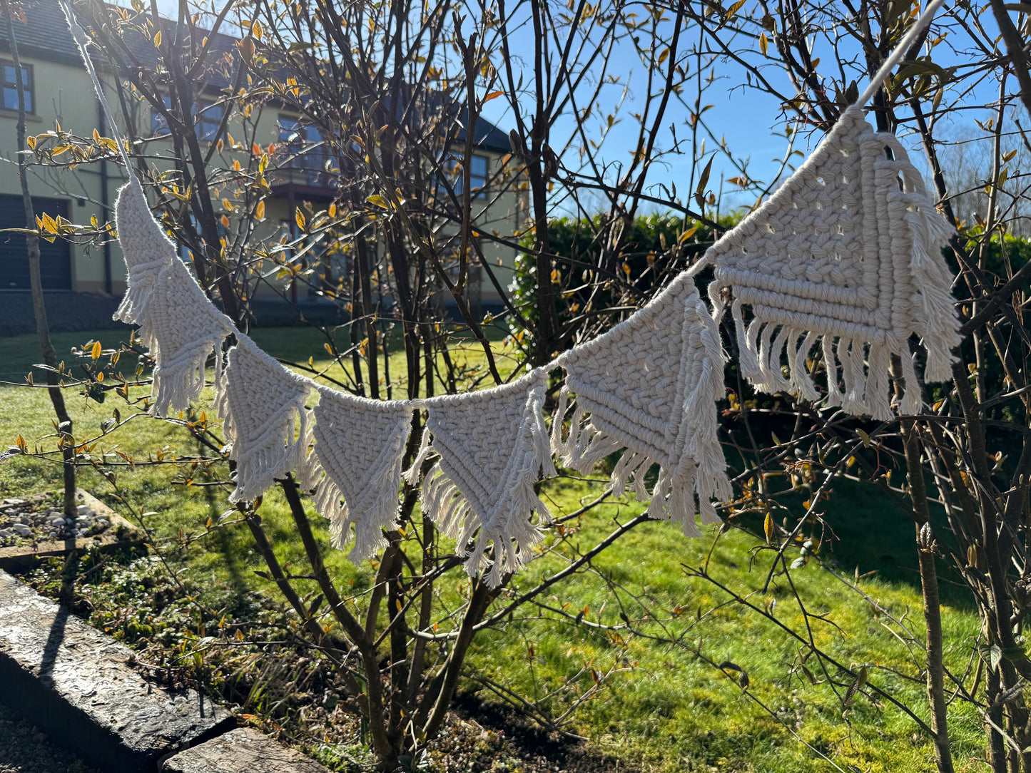 Macrame bunting hanging from branches in a garden