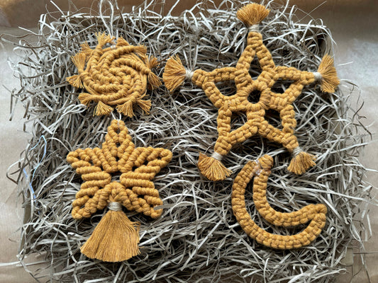 Four yellow macrame ornaments shaped like a spiral galaxy, two types of star, and a moon on a textured gray surface.