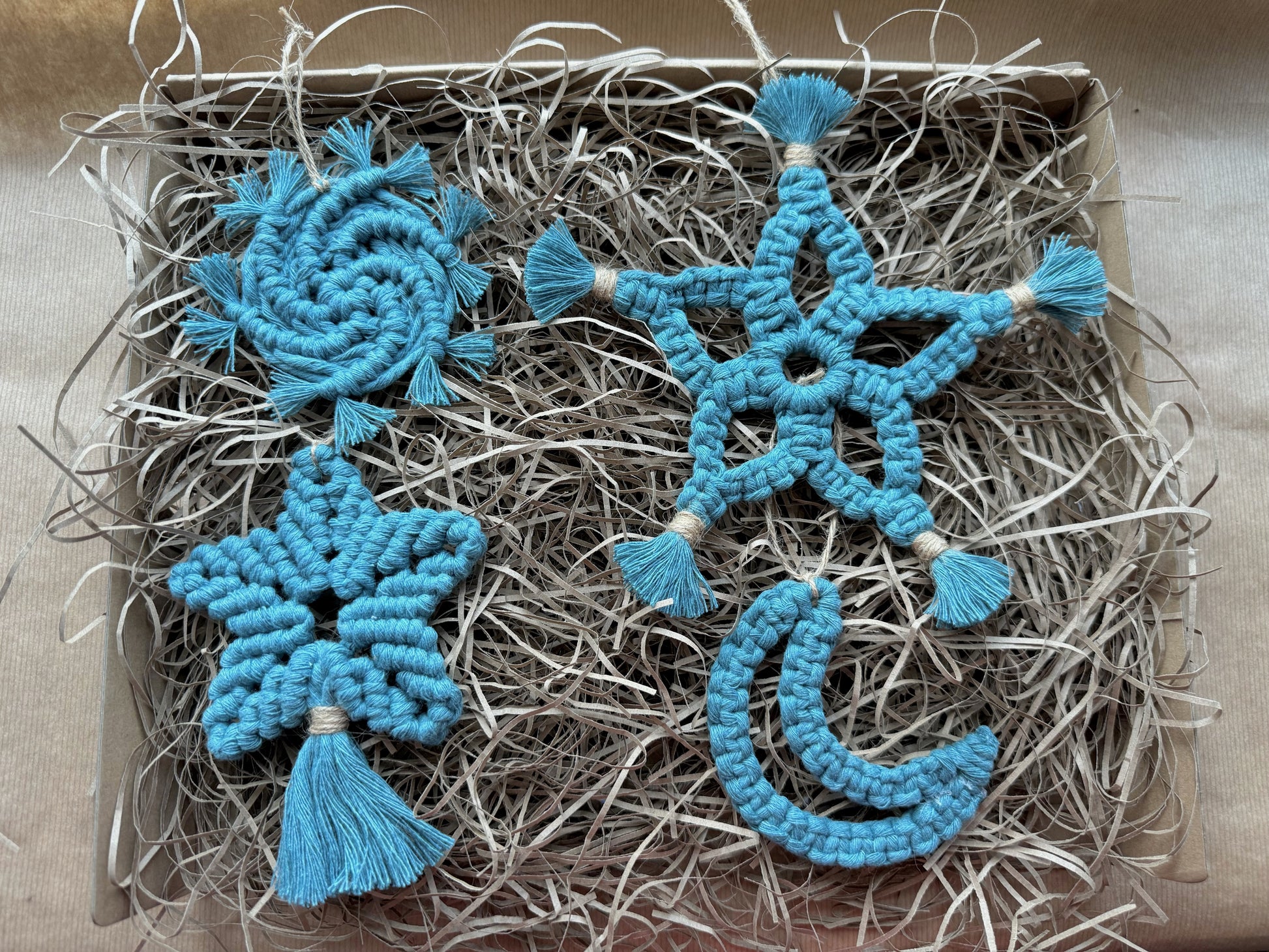 Blue macrame ornaments in a box with hay-like material