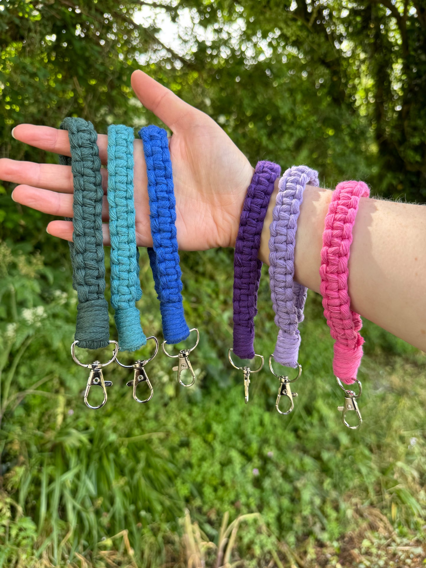 Hand holding multiple colourful macrame keychains against a natural background