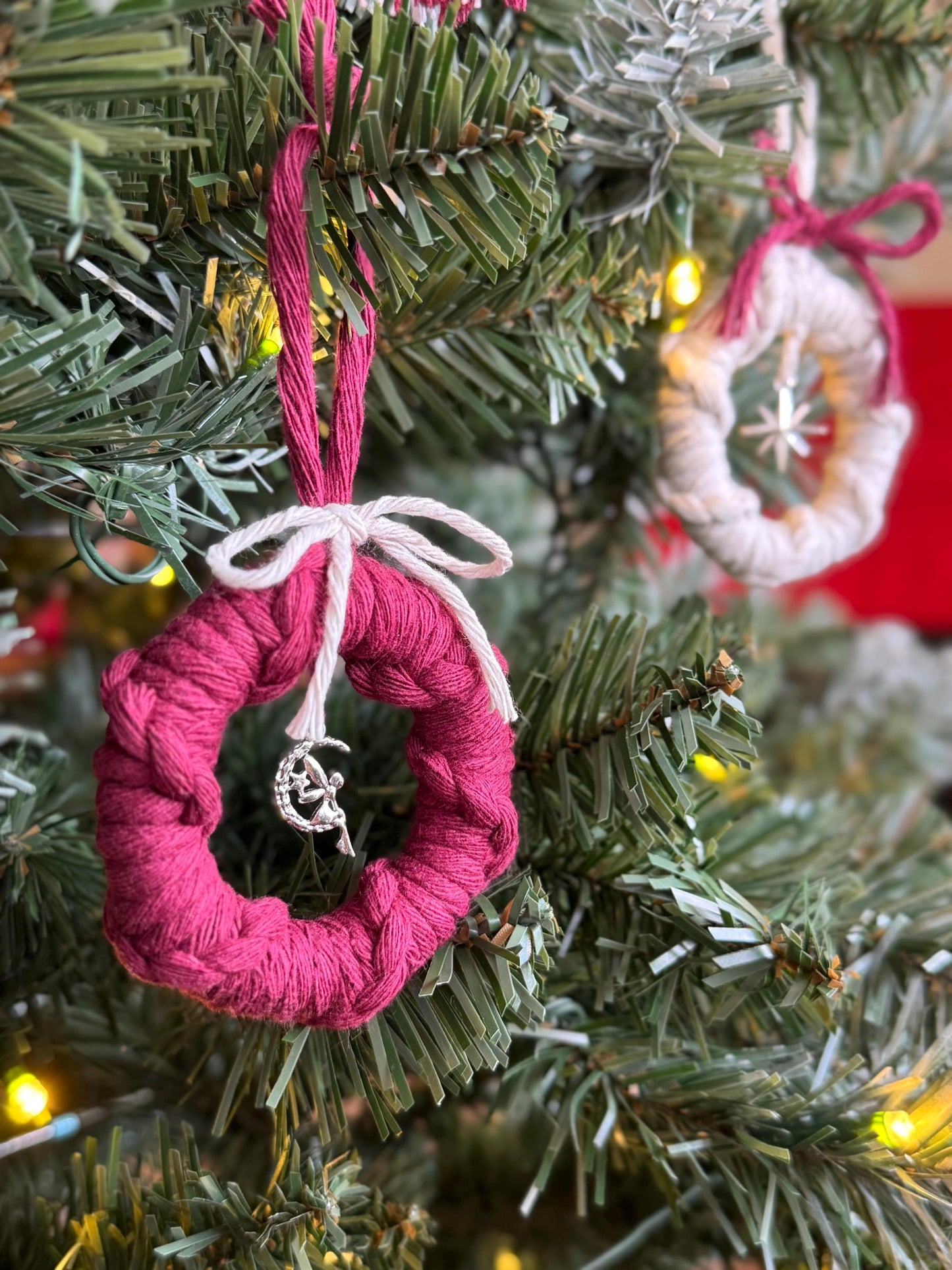 Pink yarn-wrapped ornament on a Christmas tree with blurred lights in the background