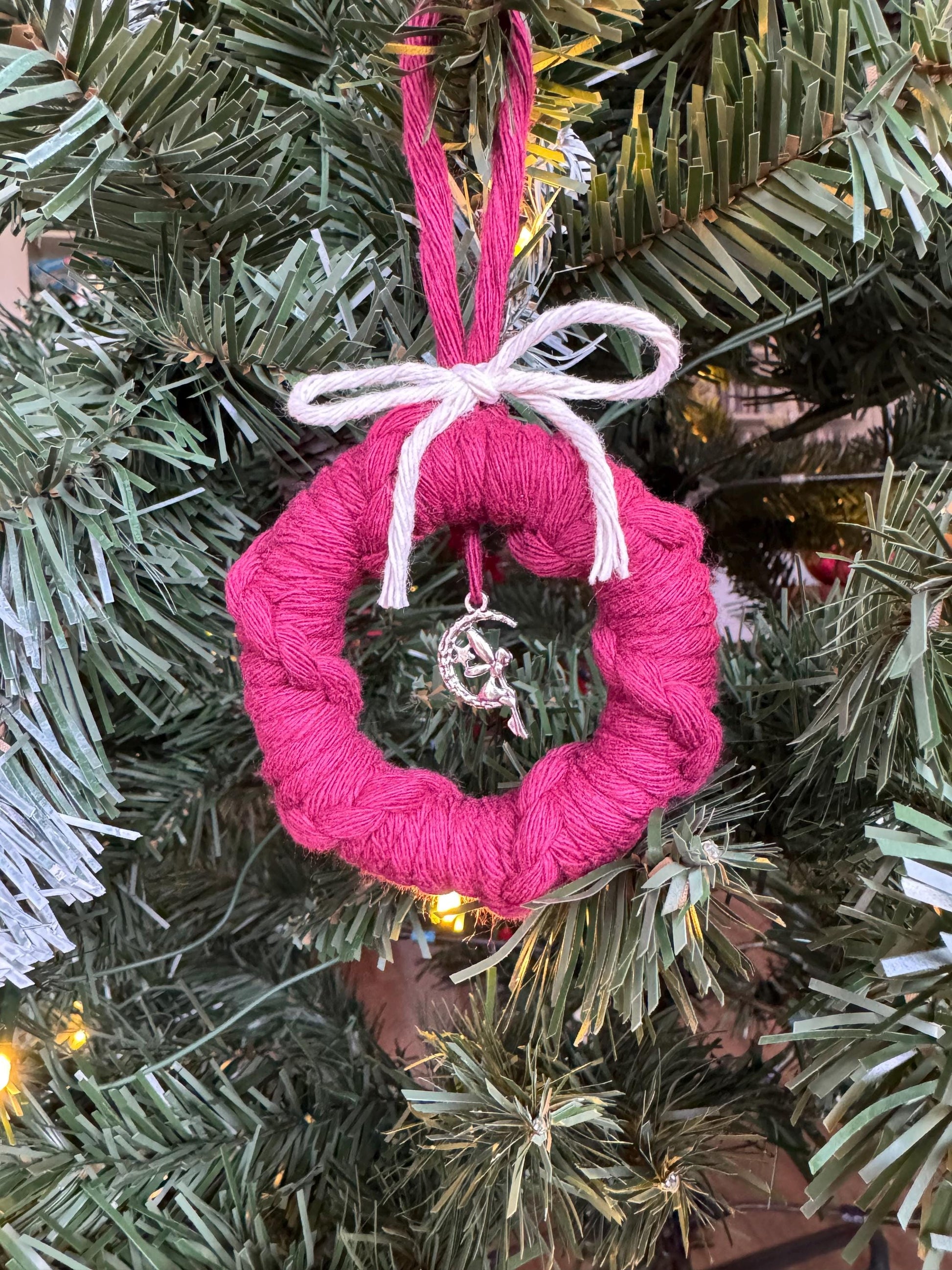 Burgundy yarn-wrapped ornament with a white ribbon on a Christmas tree.