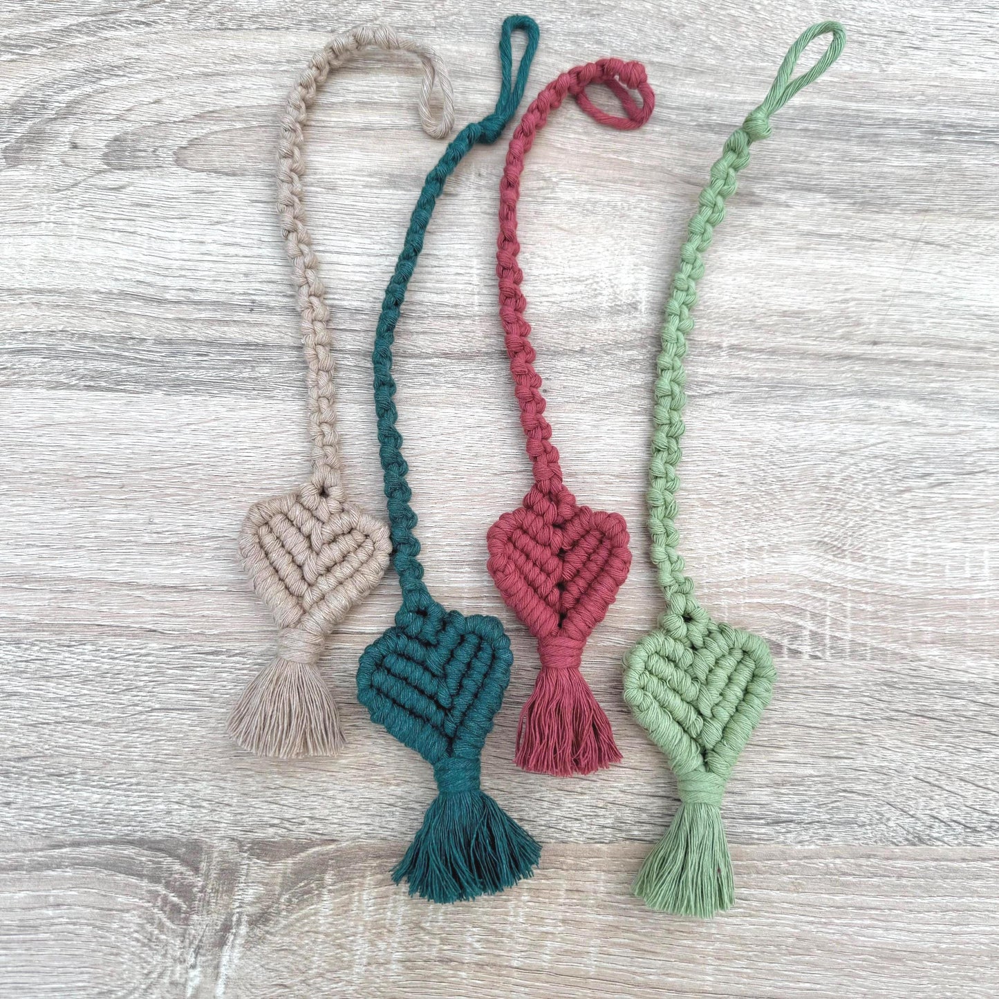 Four macrame heart-shaped bookmarks in different colors on a wooden surface