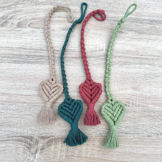Four macrame heart-shaped bookmarks in different colors on a wooden surface