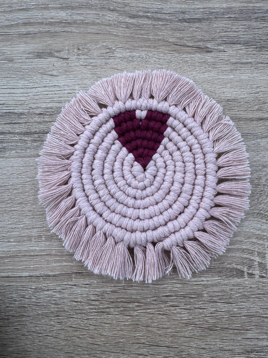Pink macrame coaster with a burgundy heart and with fringes on a wooden surface