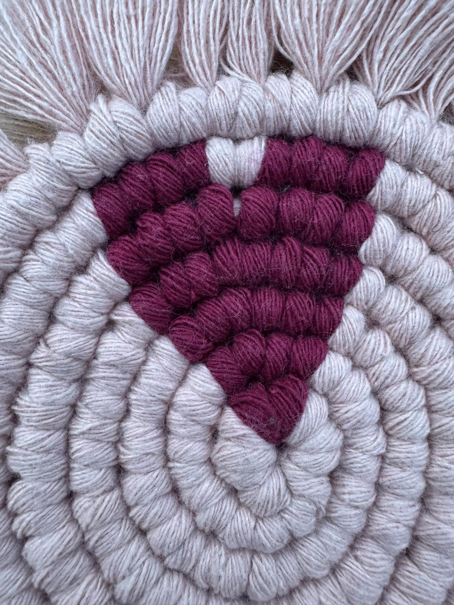 Close up of a pink macrame coaster with a burgundy heart feature