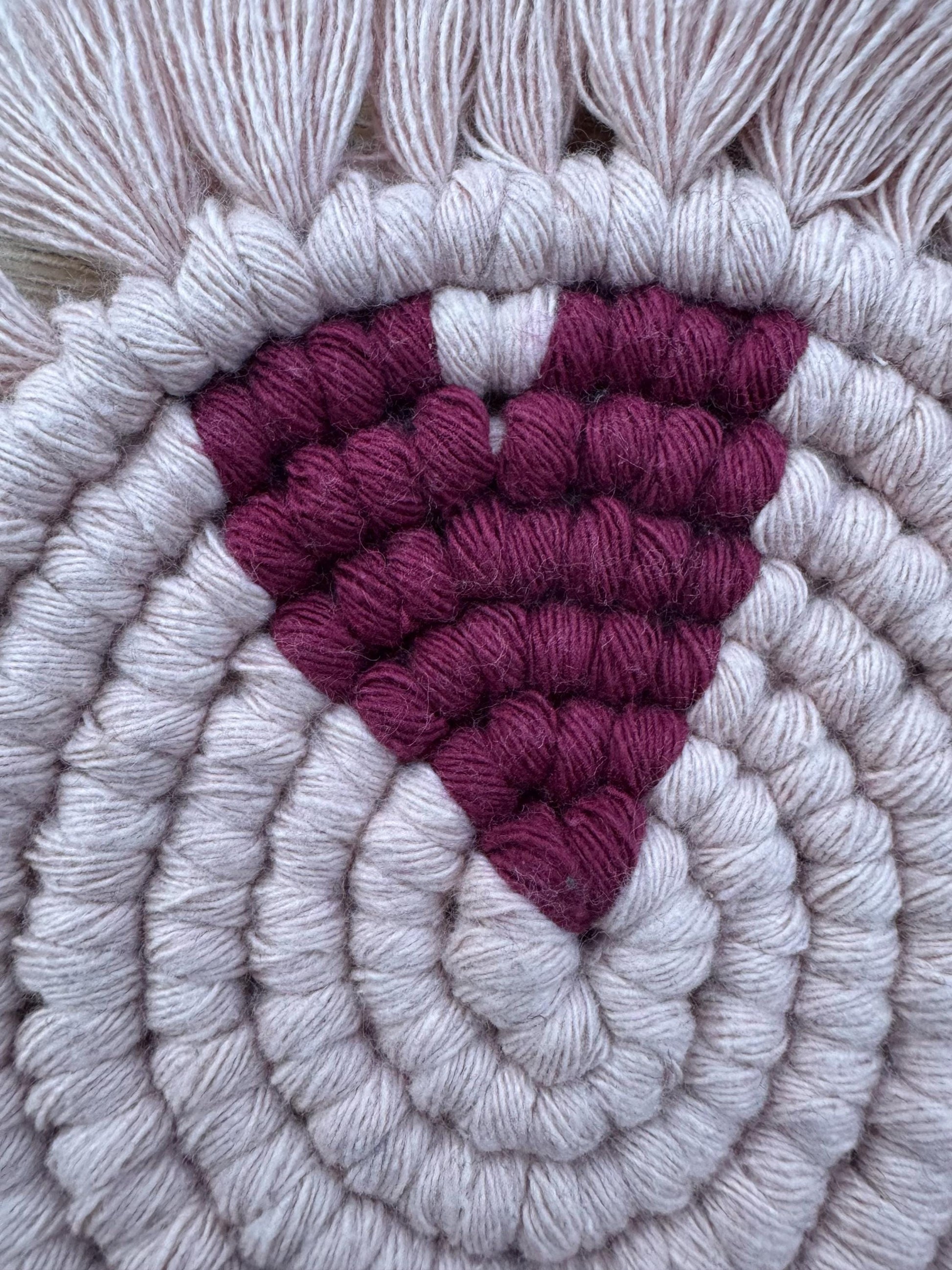 Close up of a pink macrame coaster with a burgundy heart feature
