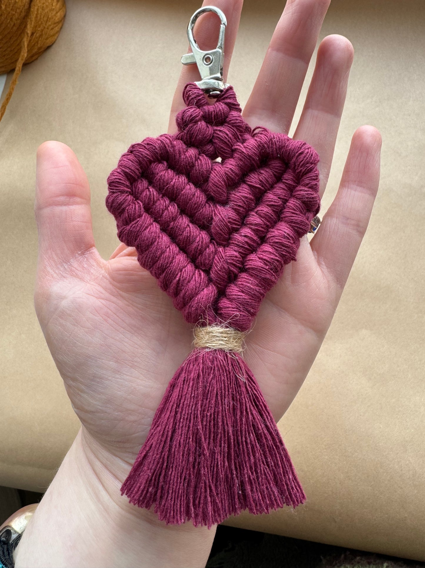 Hand holding a maroon braided keychain with a tassel against a beige background