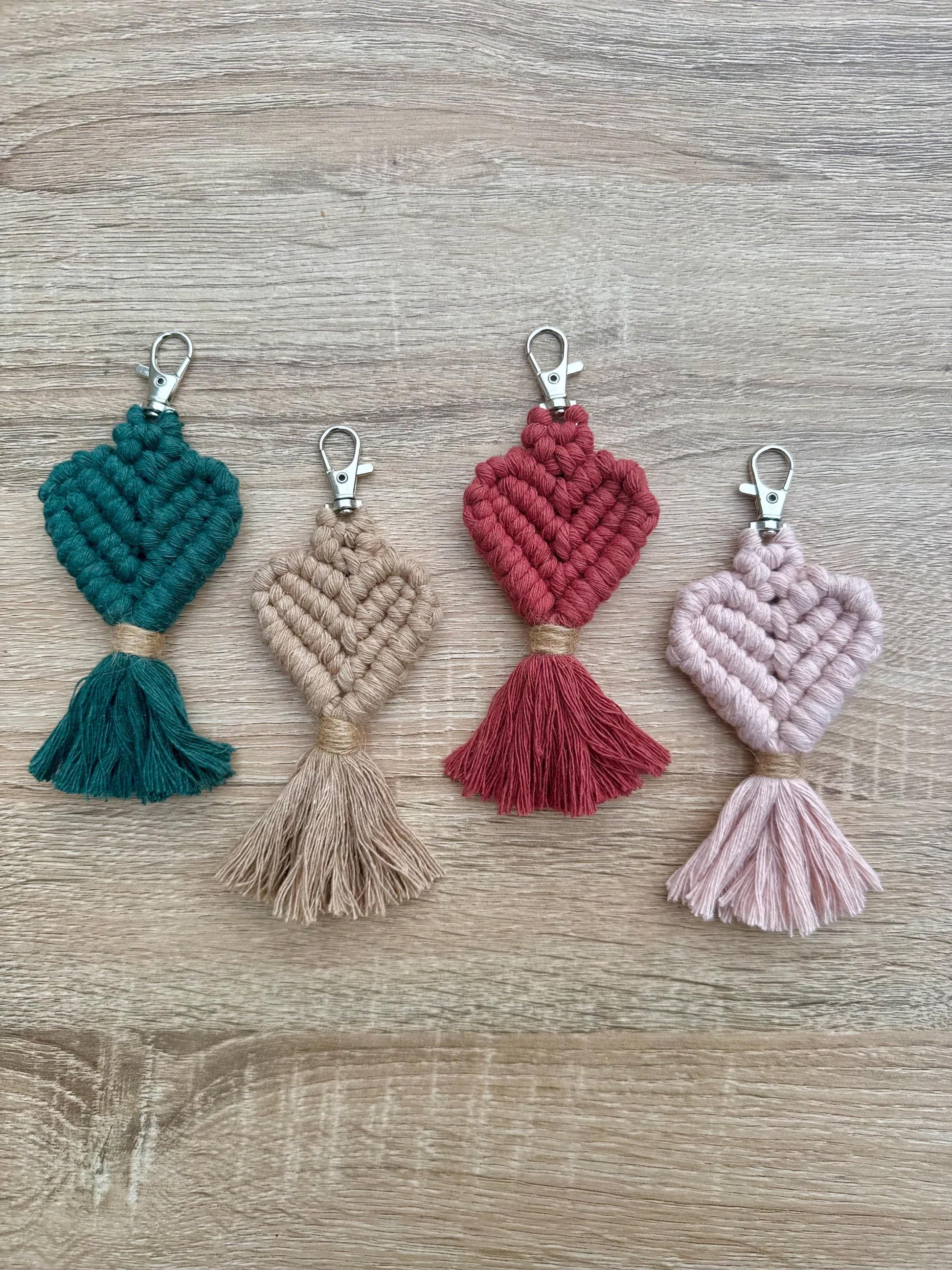 Four macrame heart-shaped keychains in different colors on a wooden surface