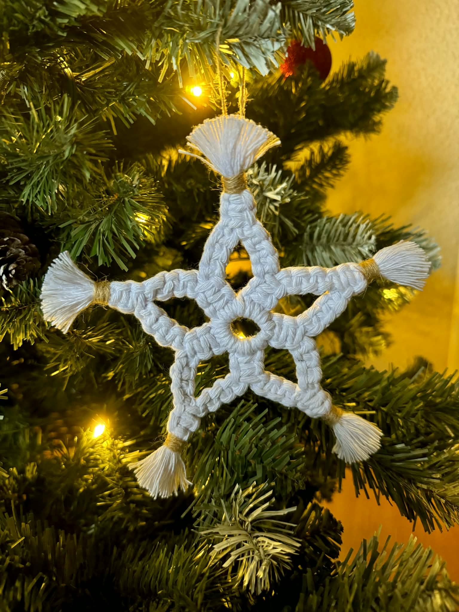 White macrame star ornament on a decorated Christmas tree with warm glow.