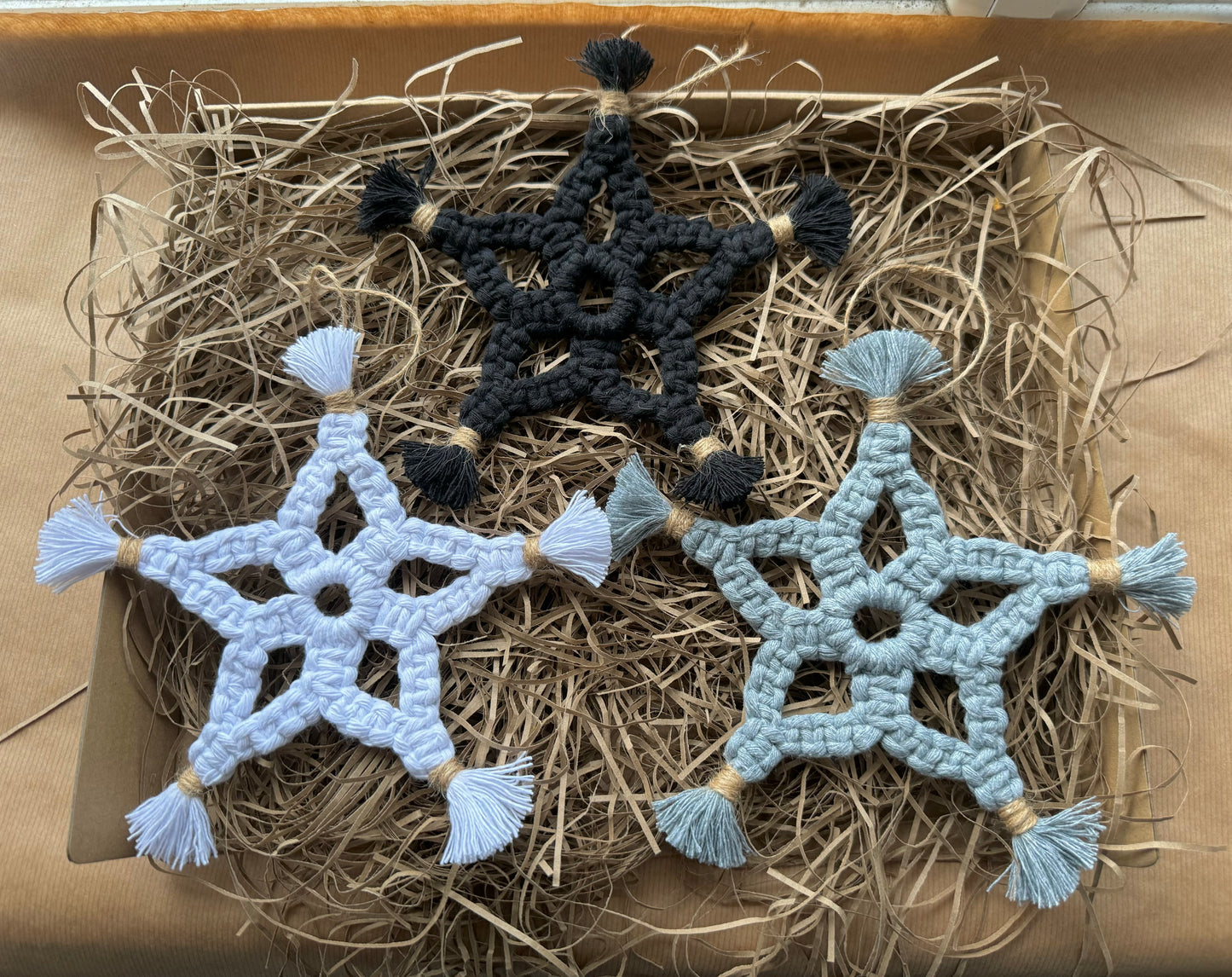 Three macrame star decorations in black, white, and gray on a bed of hay.