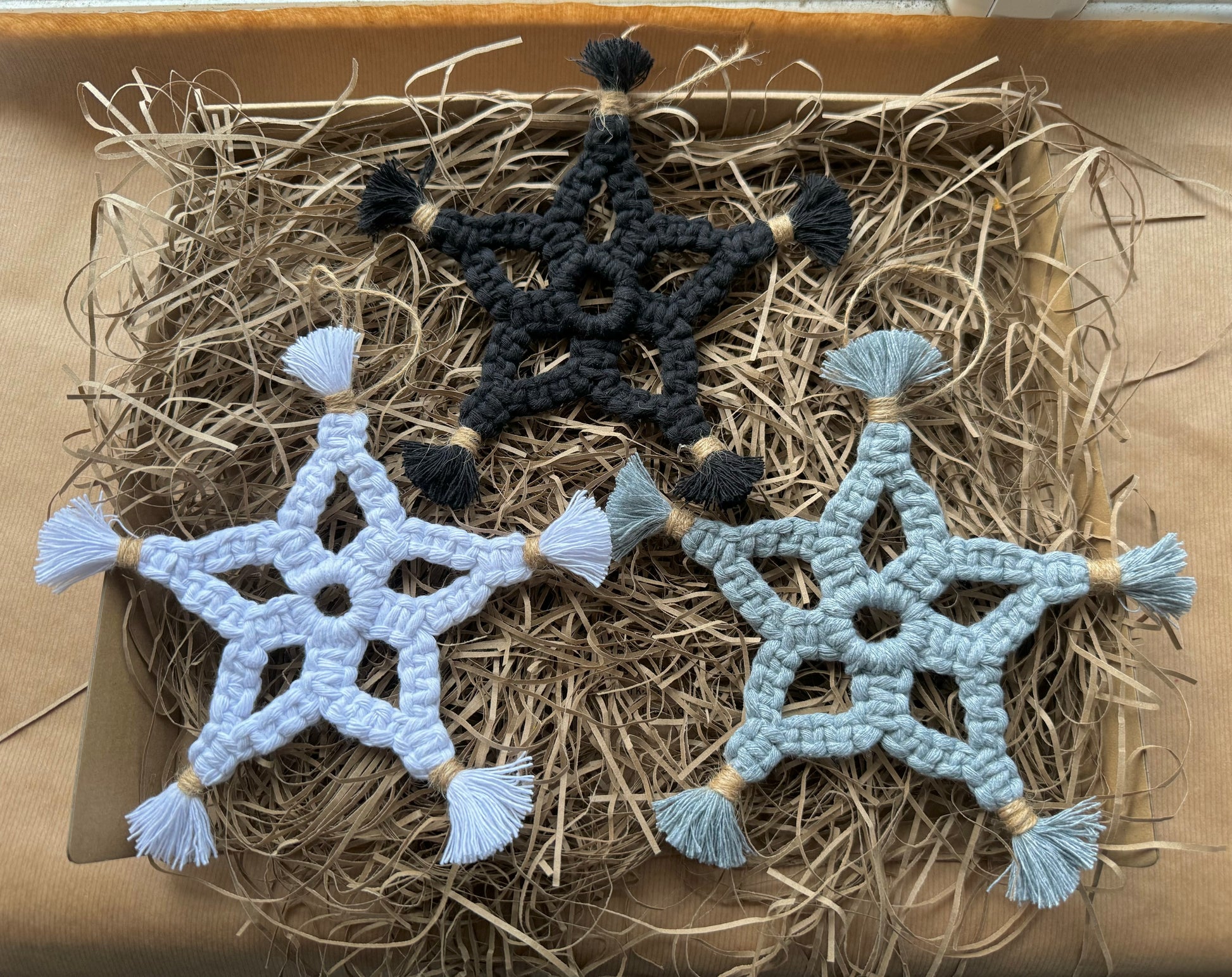 Three macrame star decorations in black, white, and gray on a bed of hay.