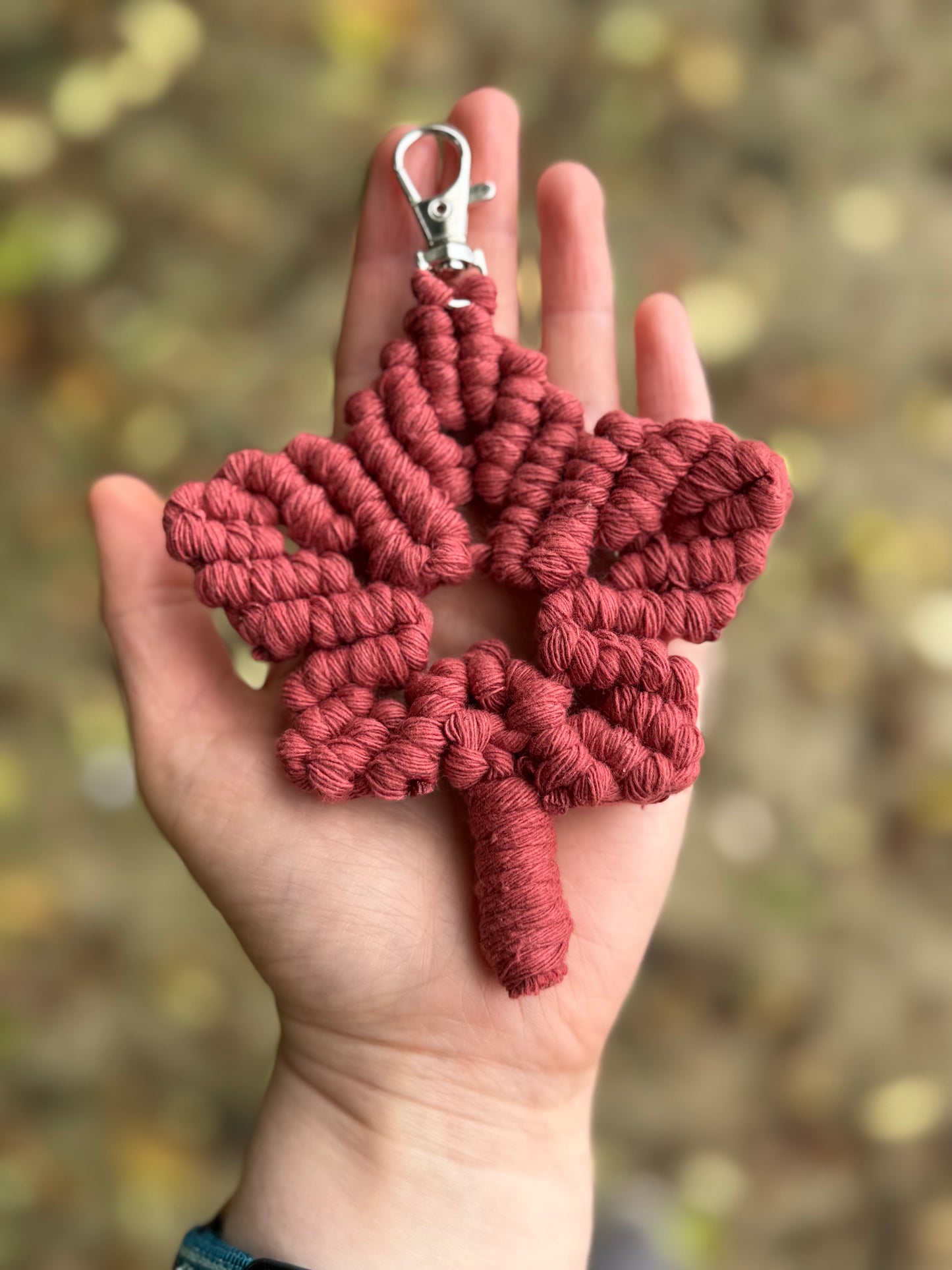 Red macrame leaf keychain held in a hand with a blurred natural background