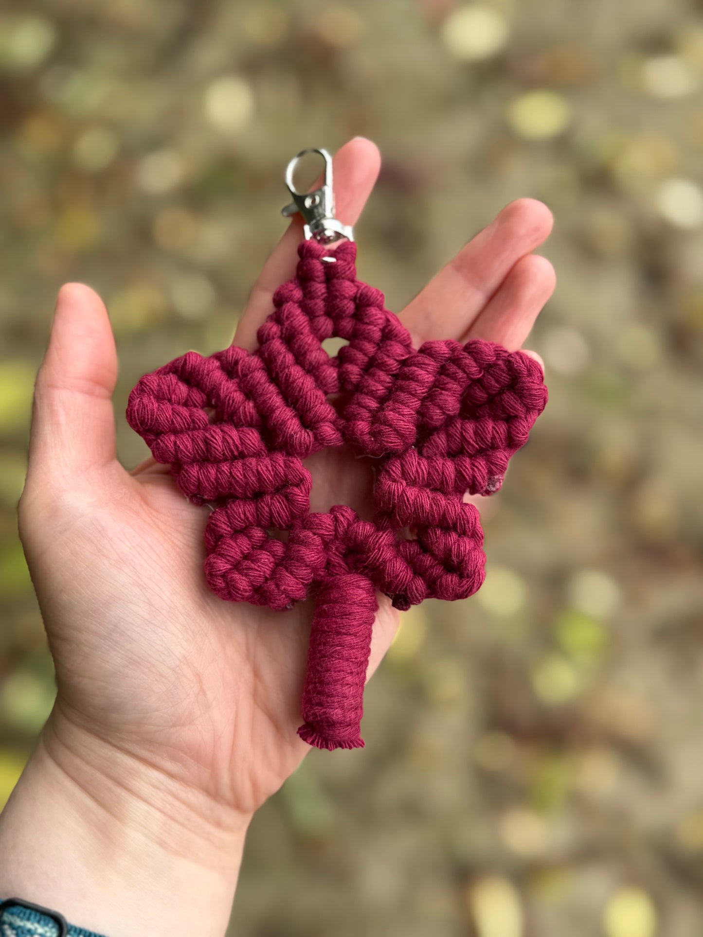 Red macrame autumn leaf keychain held in a hand with a blurred natural background