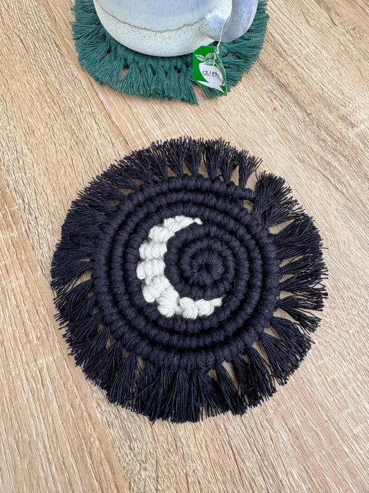 Black circular macramé coaster with white crescent moon center on a wooden surface