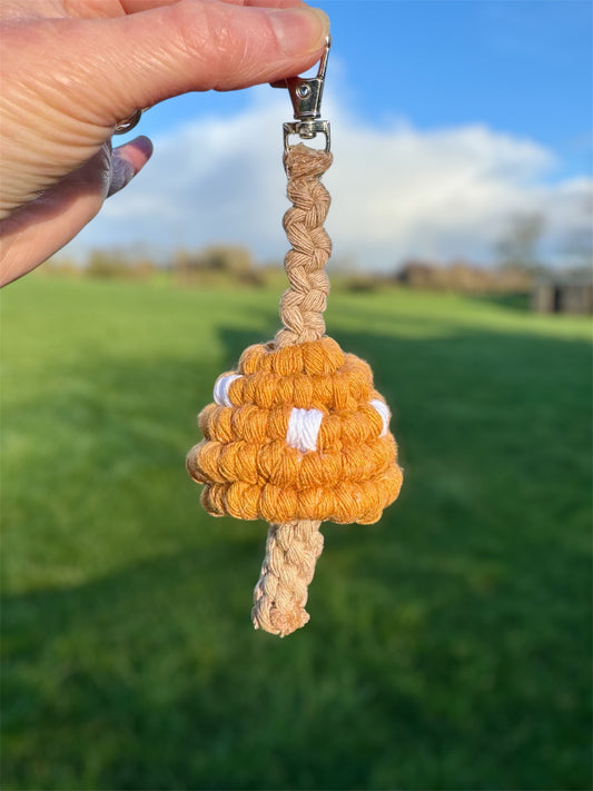 Hand holding a braided keychain with a yellow mushroom design against a blurred outdoor background