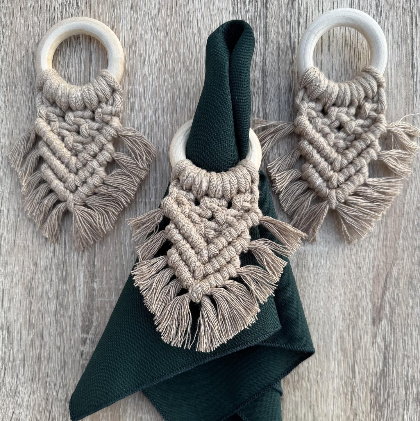 sand coloured macrame napkin rings with a dark green napkin on a wooden surface