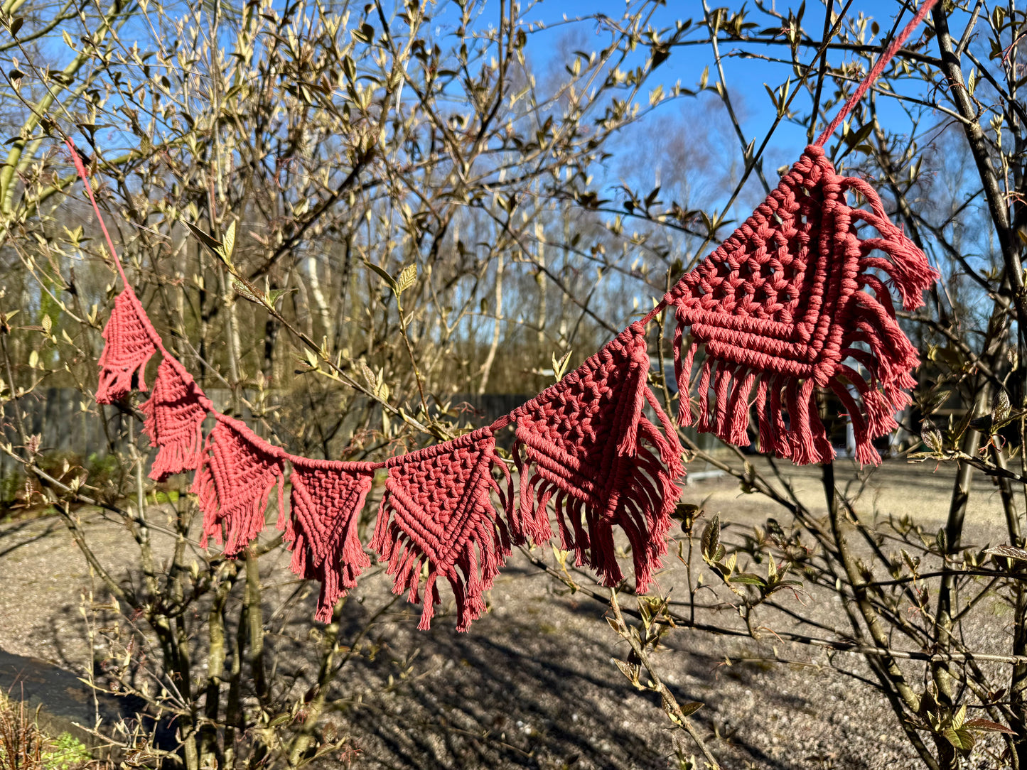 Terracotta macrame bunting outdoors with grass and trees in the background
