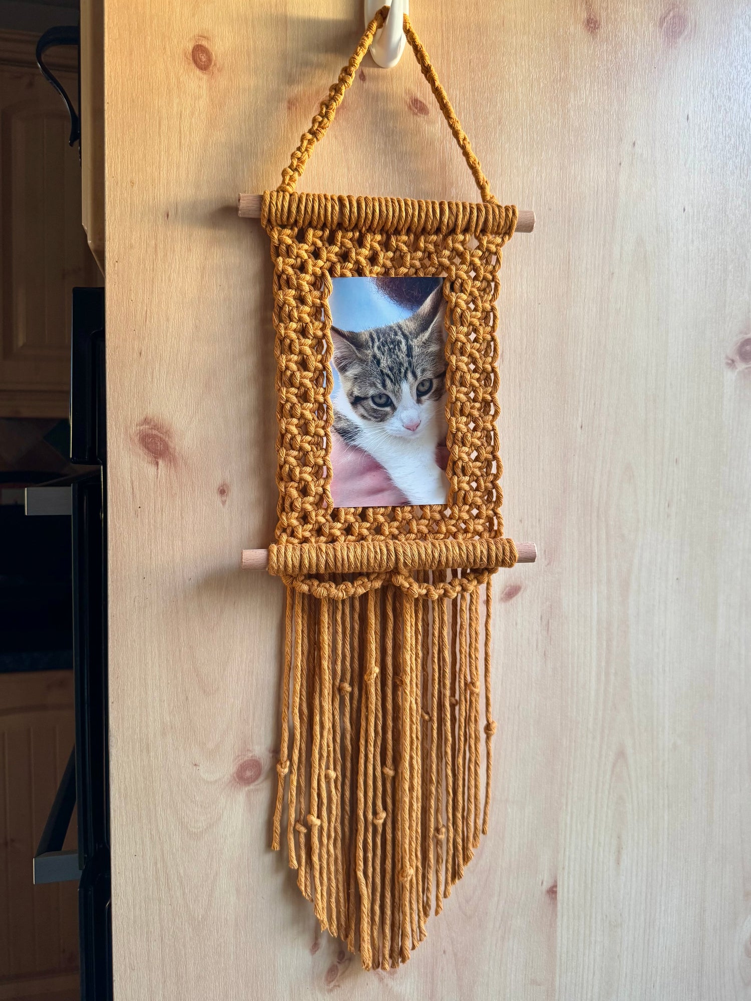 a yellow macrame photo frame with a fringe containing a photo of a cat on a wooden surface