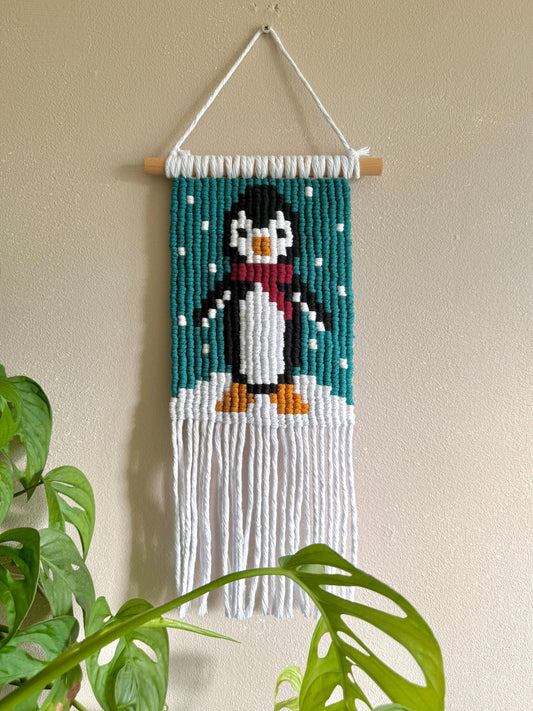 Macrame wall hanging with a penguin design on a beige wall.