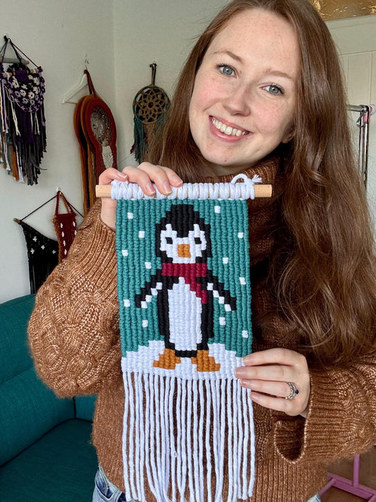 Person holding a macrame penguin artwork in a cozy room.