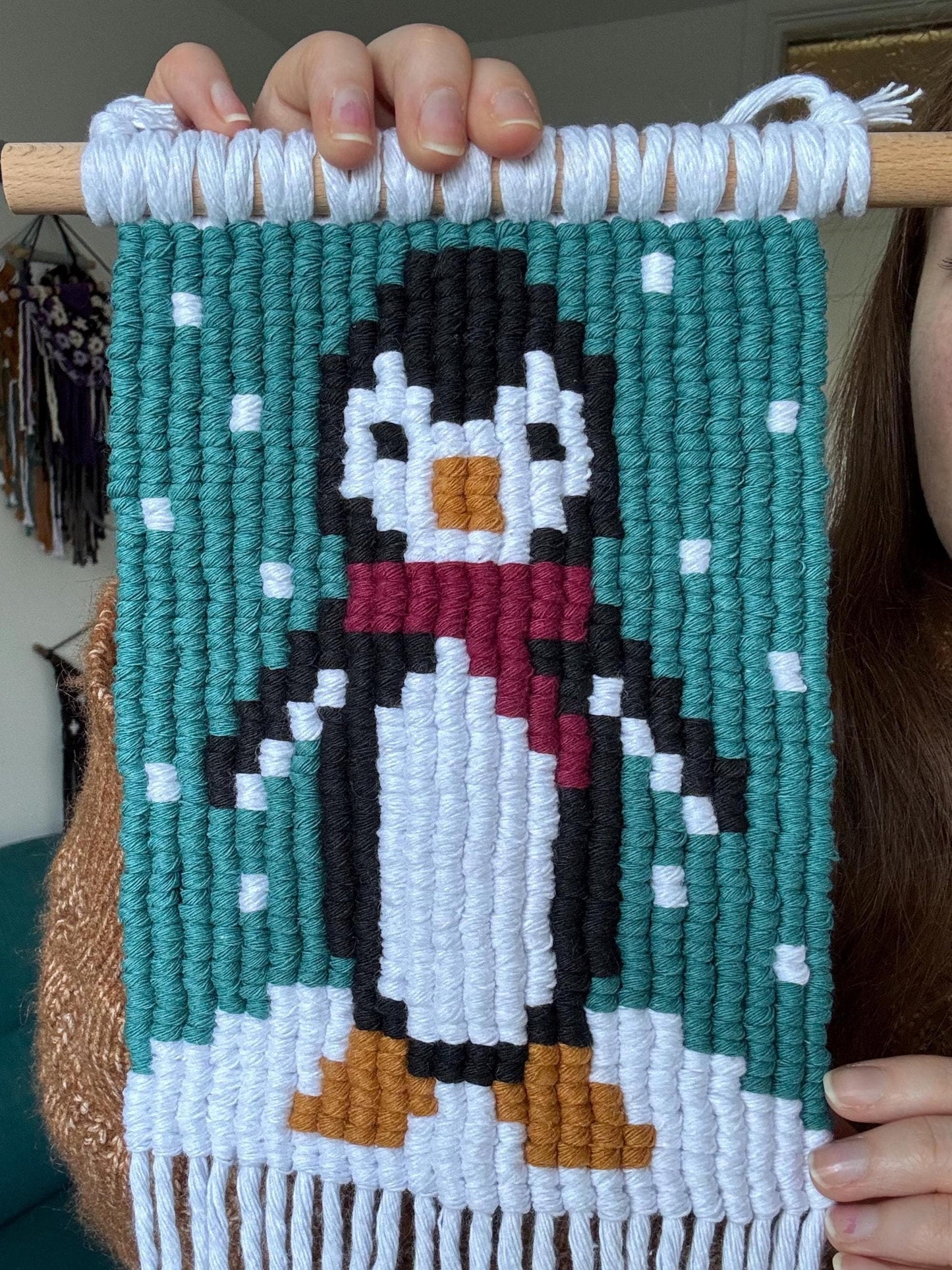 Handmade pixelated penguin design on a woven wall hanging held by a person.