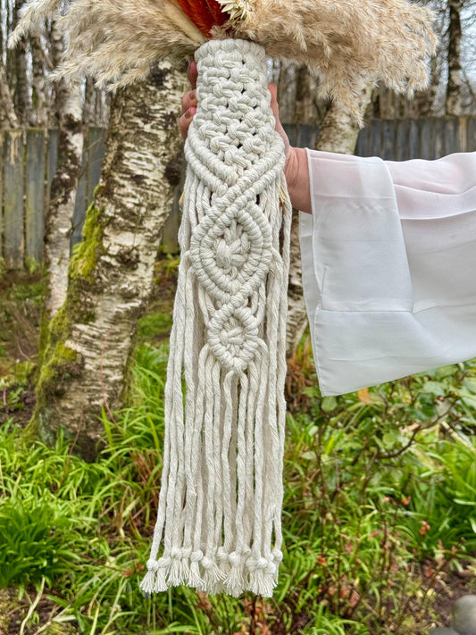 Macrame bouquet wrap held by a person outdoors with trees and grass in the background