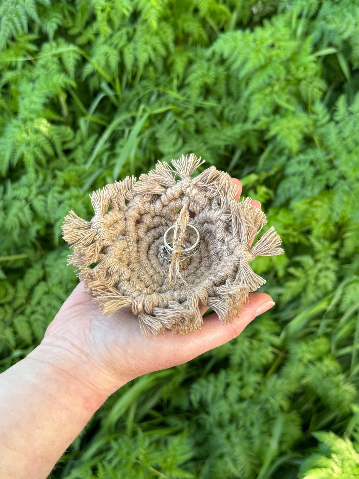 Hand holding a macrame circular ring holder with a green leafy background