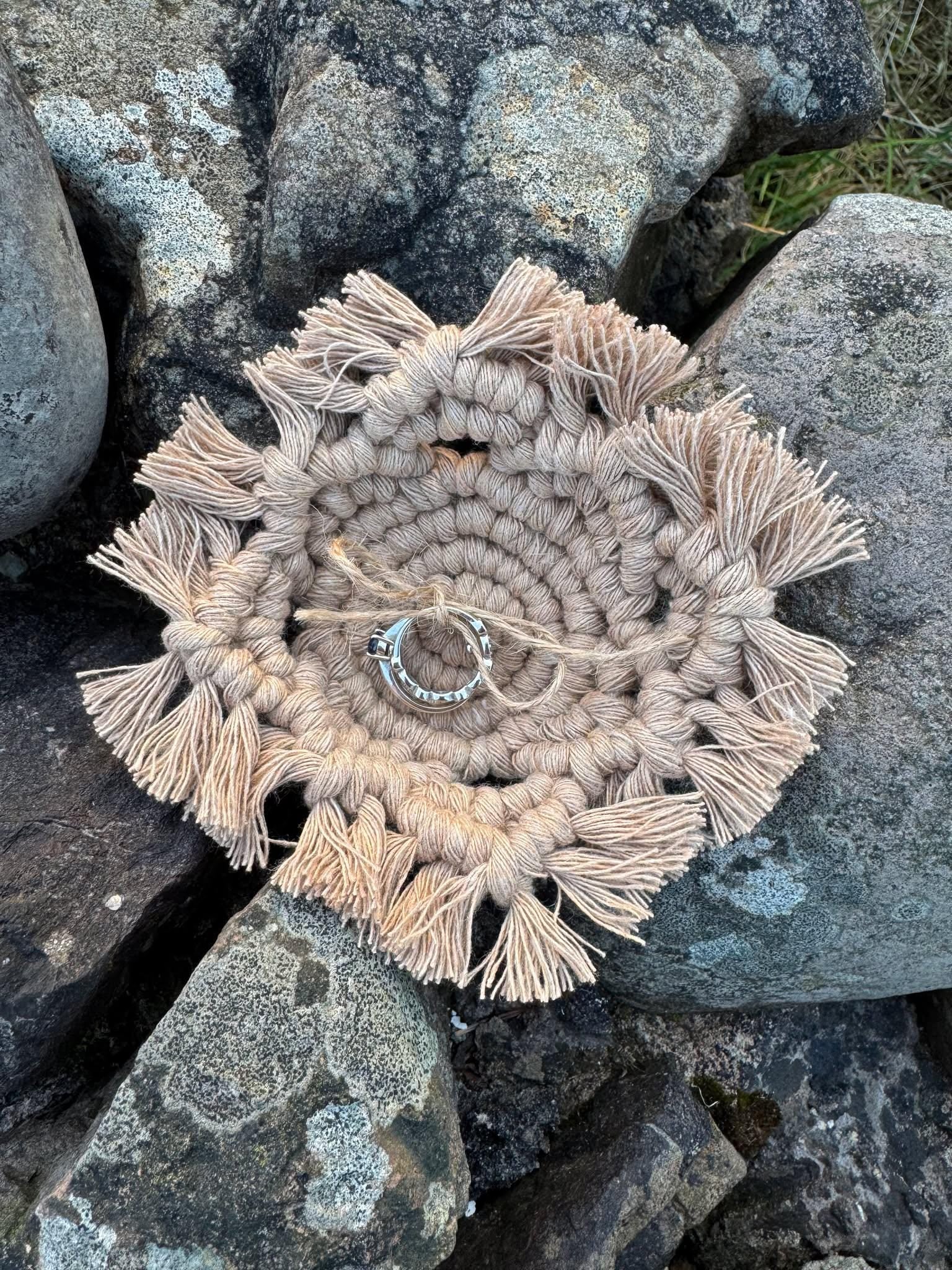 Macrame beige wedding ring cushion with tassels on a stone surface