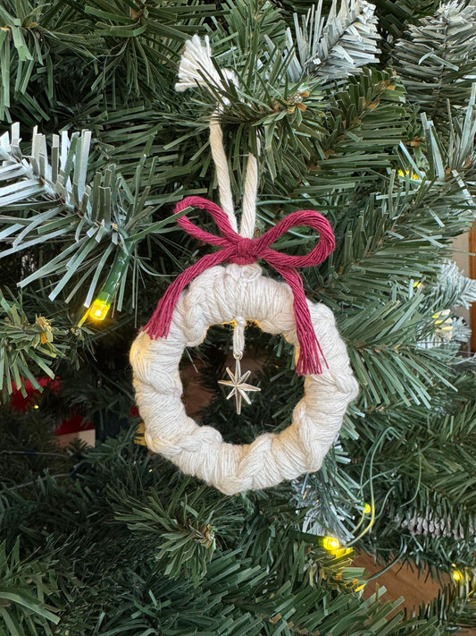 Decorative wreath ornament with a burgundy ribbon on a Christmas tree.