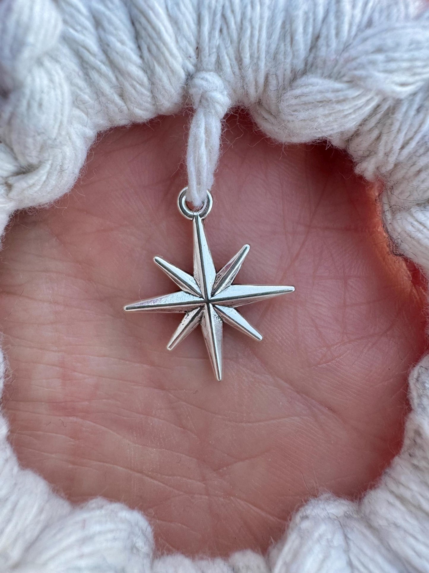 Silver star-shaped pendant held in a hand against a textured white background