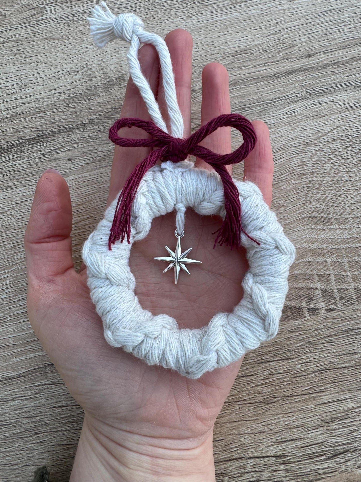 Hand holding a white macrame ornament with a star charm and red bow on a wooden surface