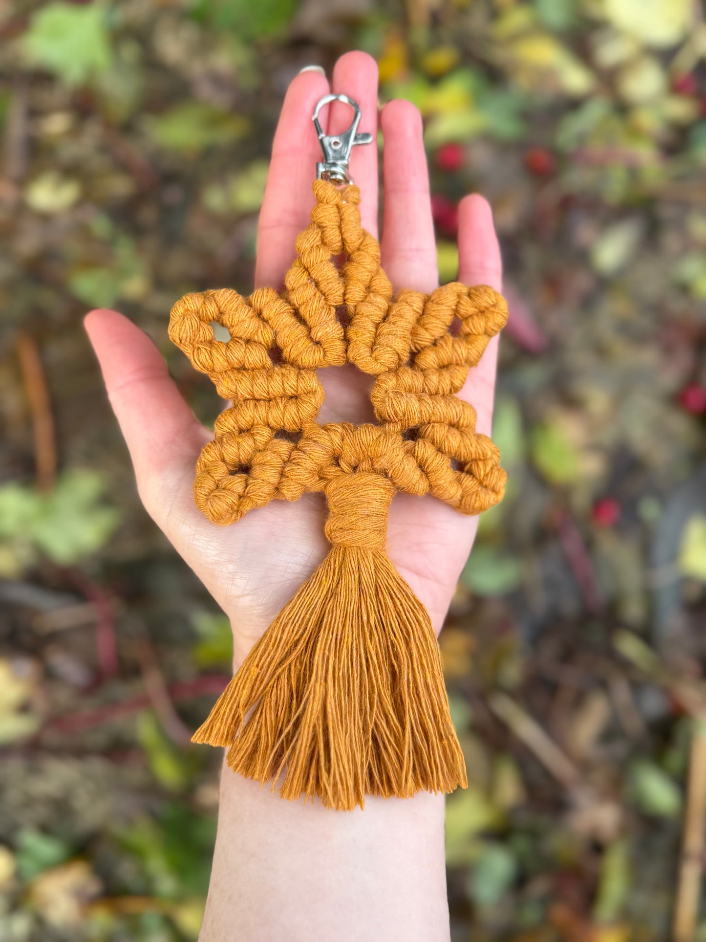 Hand holding a yellow star-shaped macrame keychain with tassel against a blurred natural background