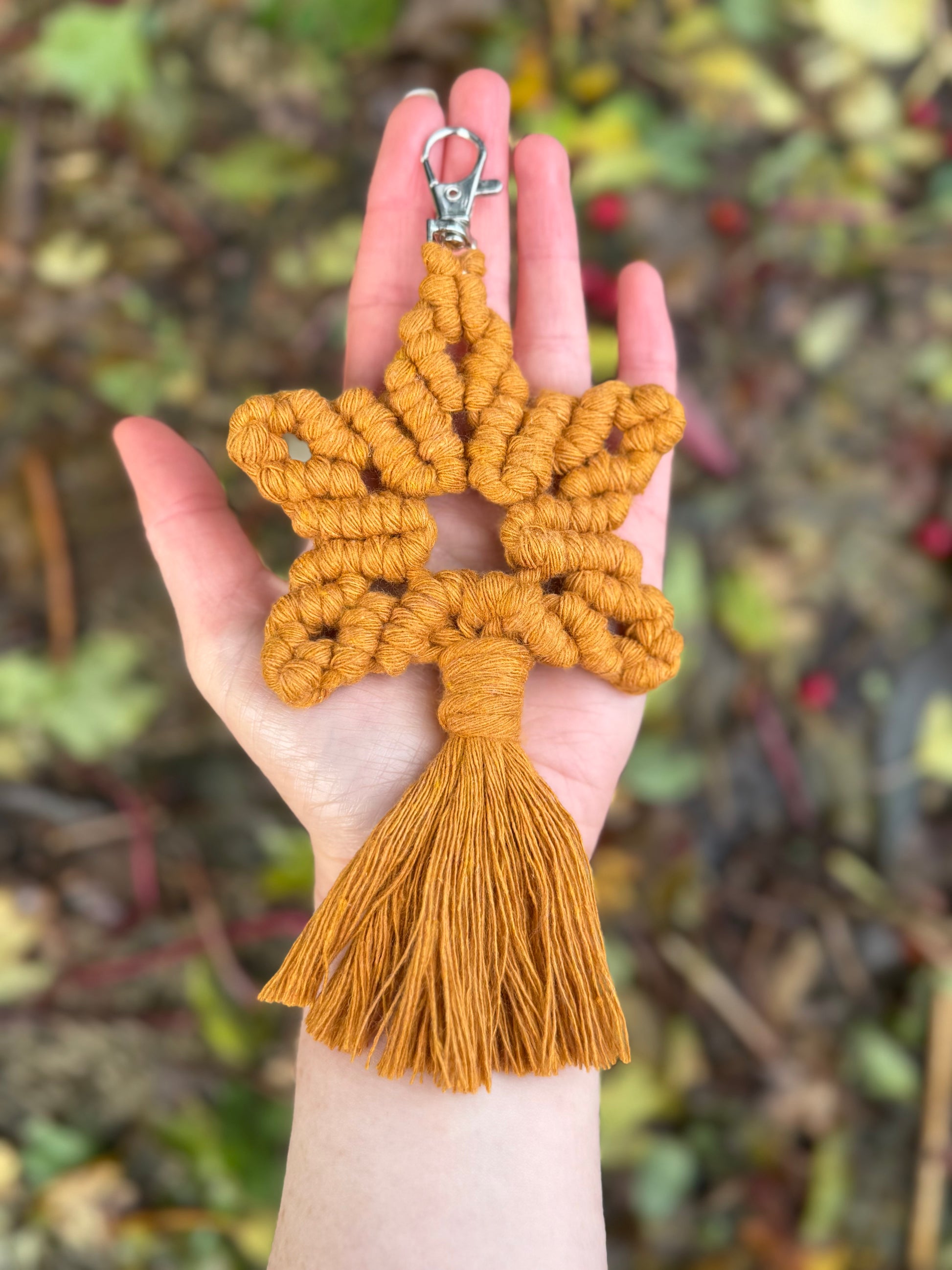 Hand holding a yellow star-shaped macrame keychain with tassel against a blurred natural background