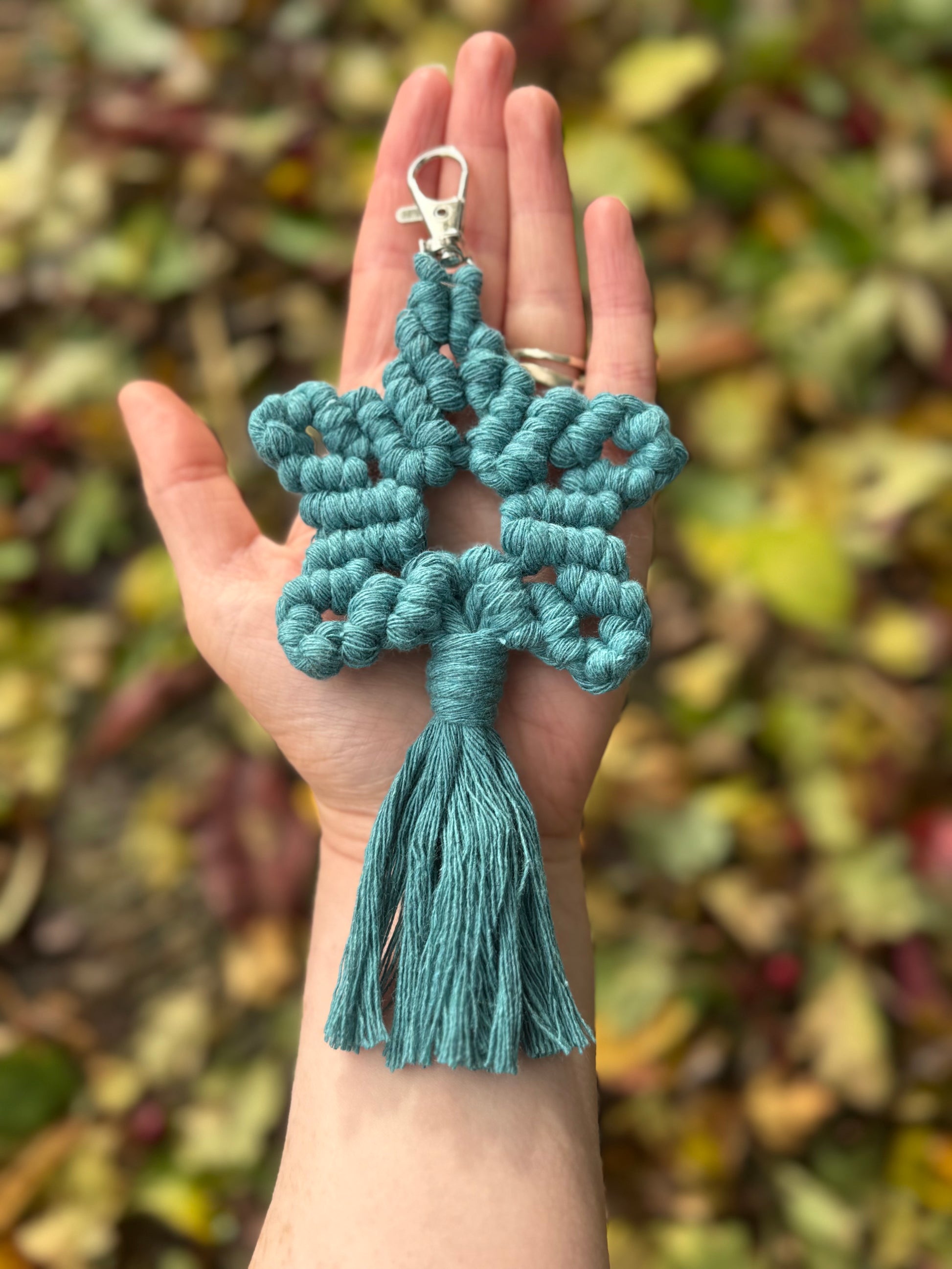 Teal braided keychain held in a hand with a blurred natural background